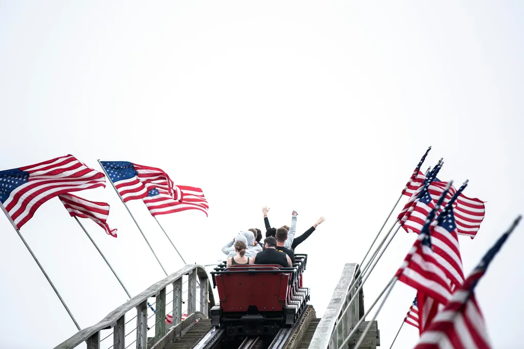 People riding a rollercoaster with their hands up, surrounded by American flags.