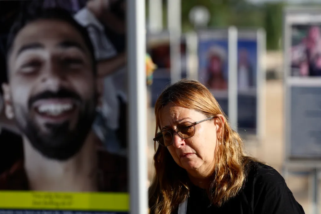 A woman with brown hair and sunglasses cries next to a large photo of a smiling man at the Nova music festival memorial.