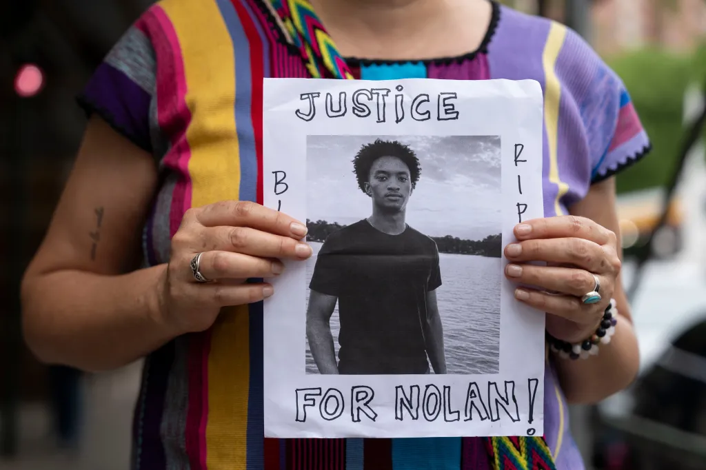 A person holding a photo of Nolan Xavier Wells with "Justice for Nolan" and "RIP" written on the sign.