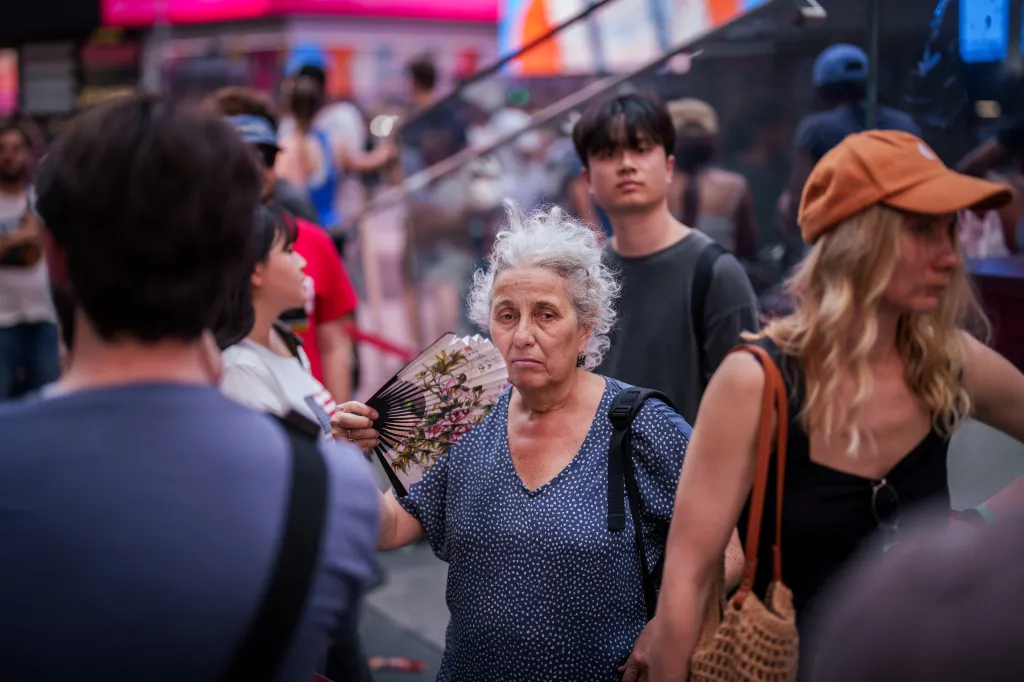 A person in a blue polka-dotted shirt uses a fan during a heat advisory in Times Square.