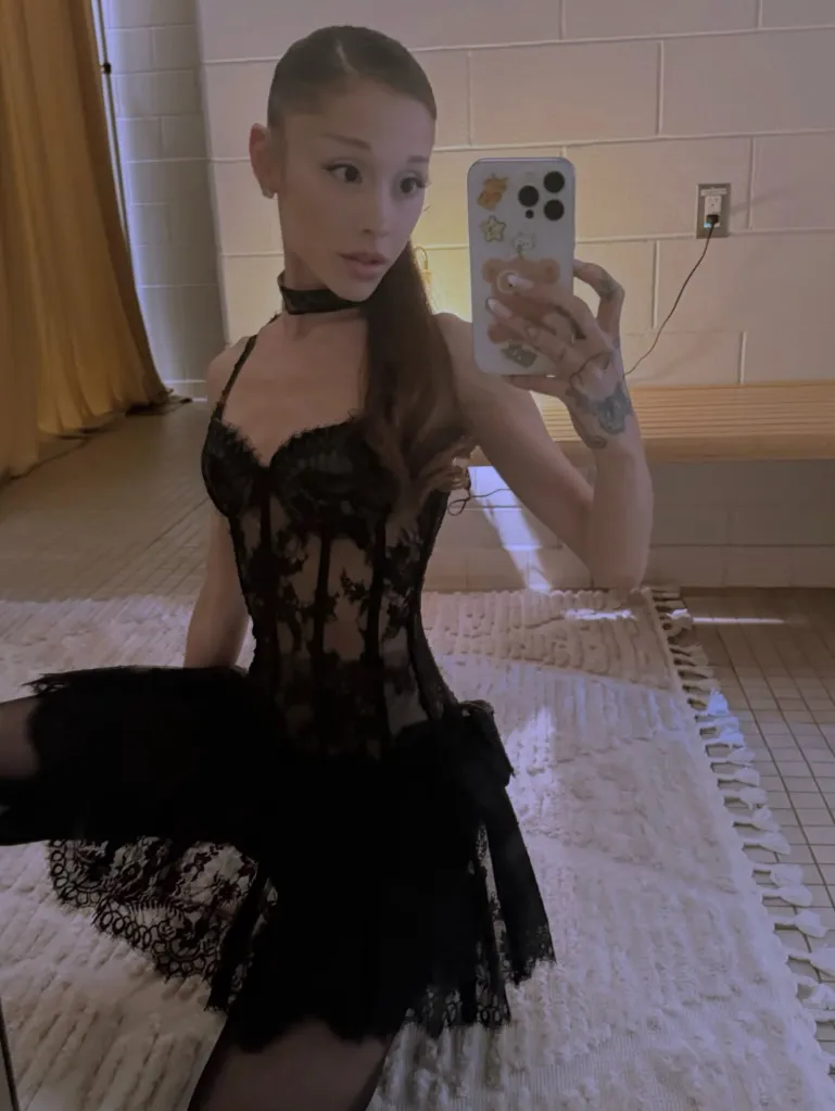 Ariana Grande taking a mirror selfie while wearing a black lace dress.