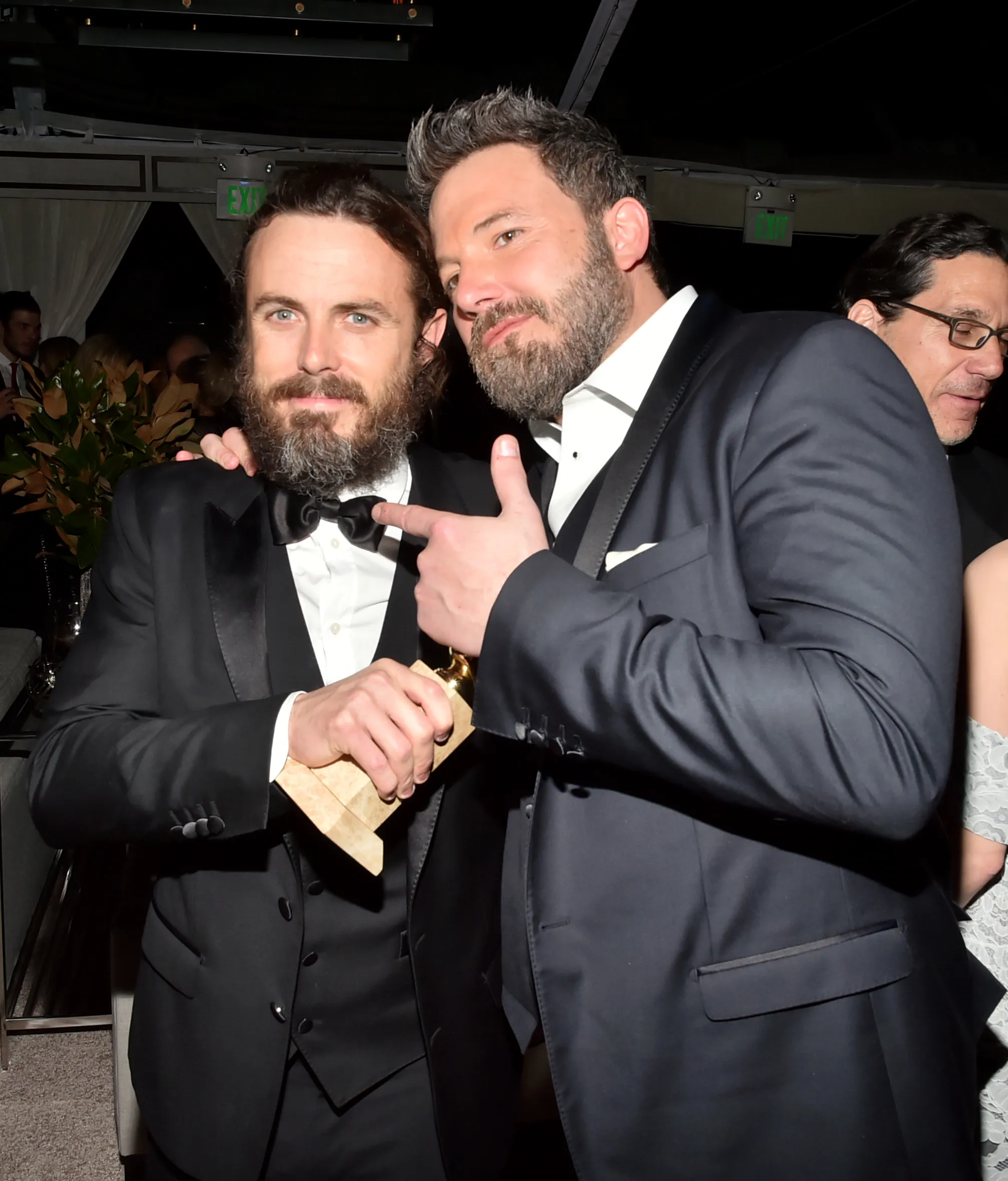 Casey Affleck and Ben Affleck smiling, Casey holding a golden award and Ben pointing to it.