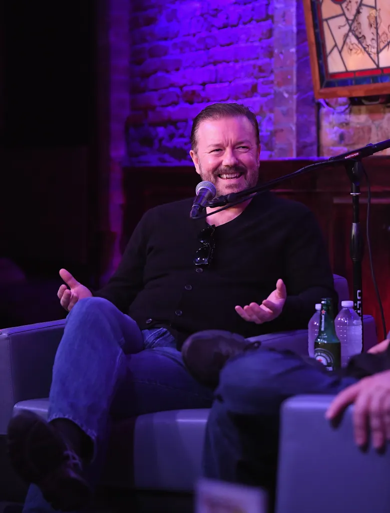 Ricky Gervais smiling while speaking into a microphone.