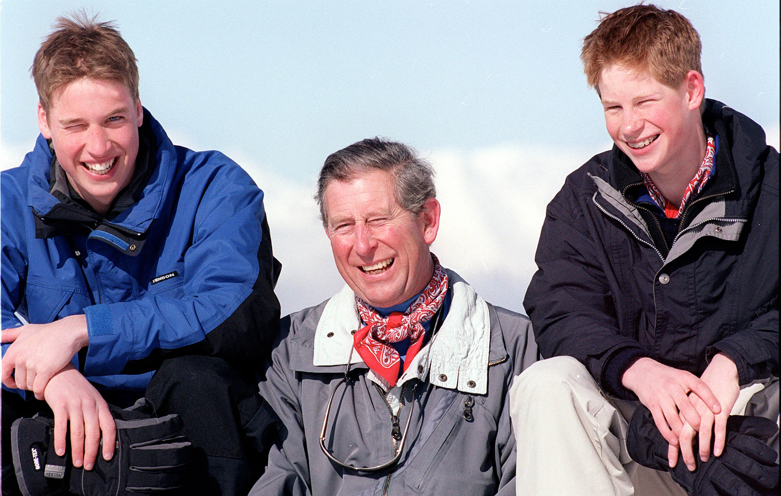 King Charles and his sons, Prince William and Prince Harry, smiling on vacation.
