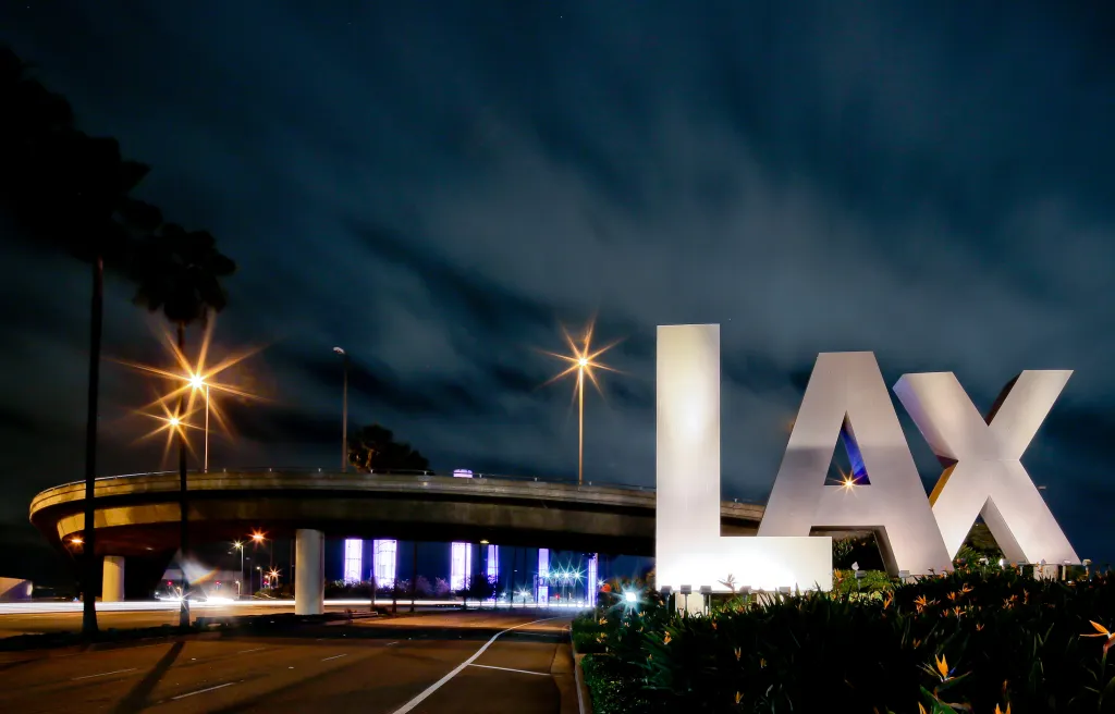 LAX sign illuminated at night next to a highway overpass.