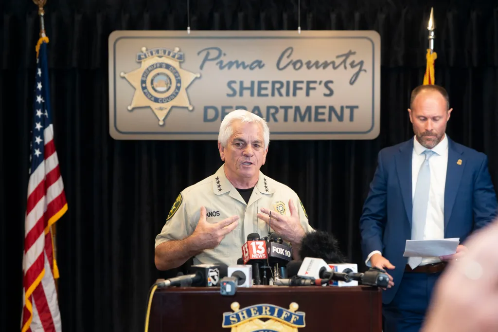 Pima County Sheriff Chris Nanos speaks at a press conference, with a deputy nearby.