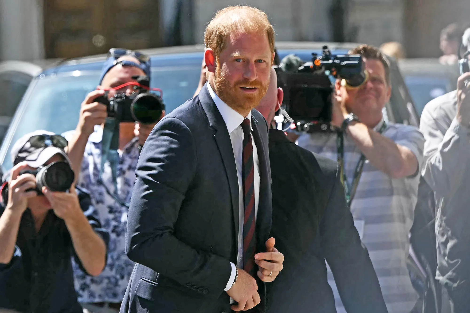 Prince Harry, Duke of Sussex, walks past several photographers with cameras and video cameras.
