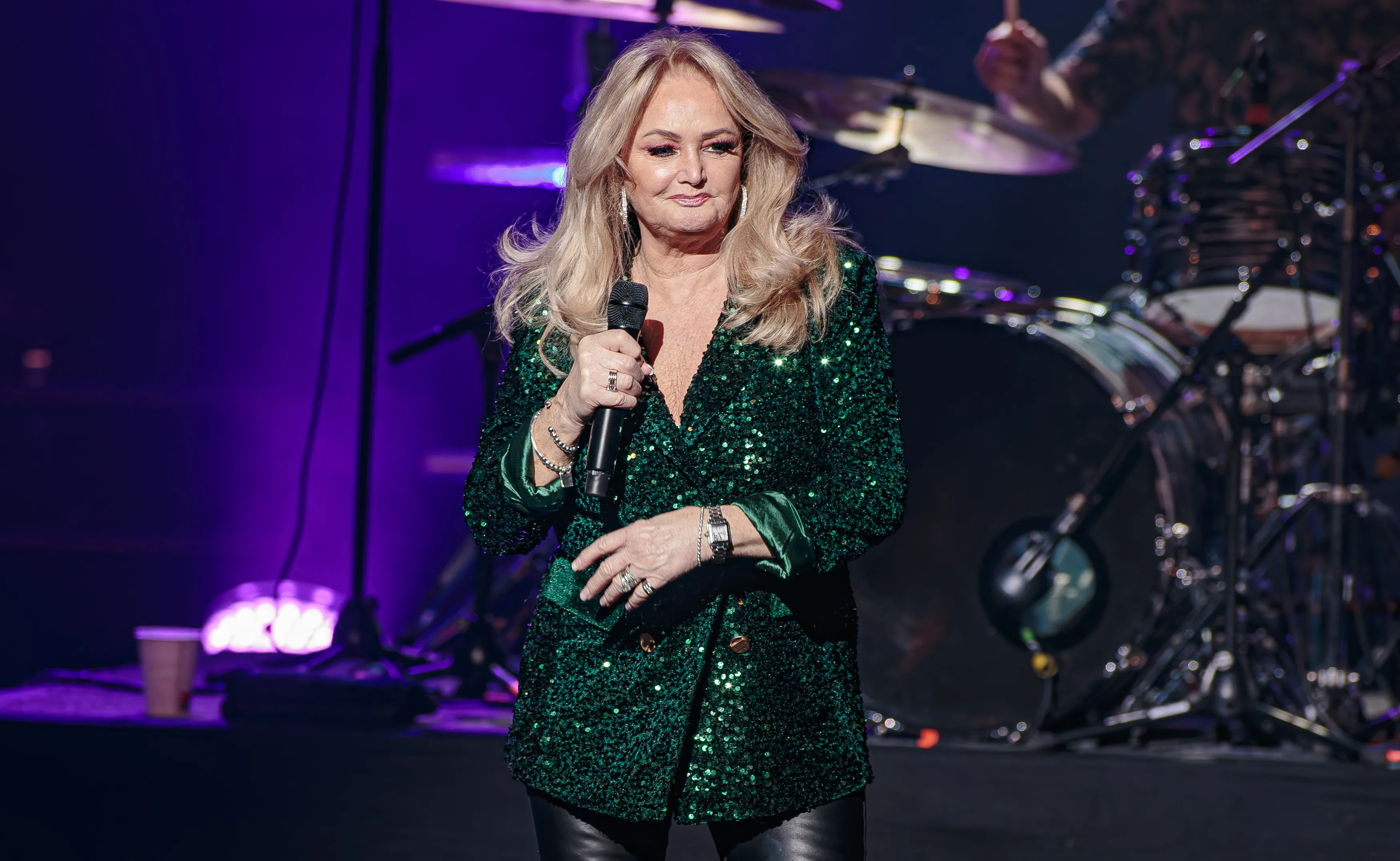 Bonnie Tyler on stage wearing a sparkling green jacket, holding a microphone.