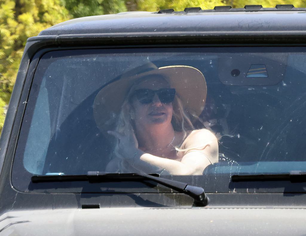 Britney Spears as a passenger in a black Mercedes-Benz, wearing a wide-brim straw hat and dark sunglasses.