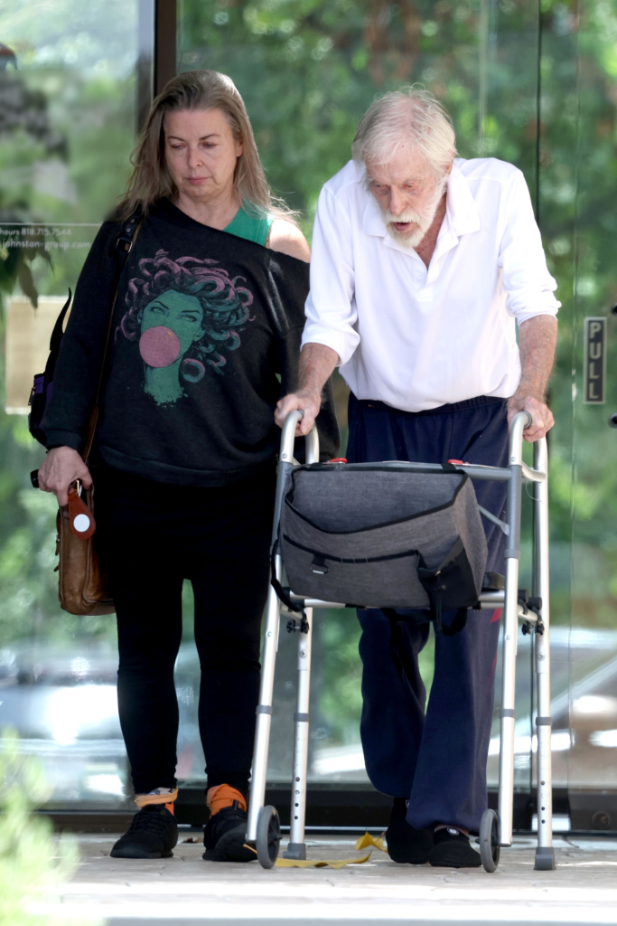 Arlene Silver and Dick Van Dyke, who is using a walker, exiting a building.