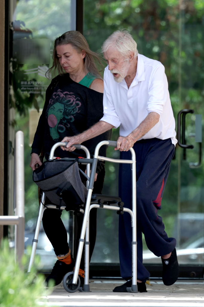 Dick Van Dyke, assisted by his wife Arlene, uses a walker while exiting a building.