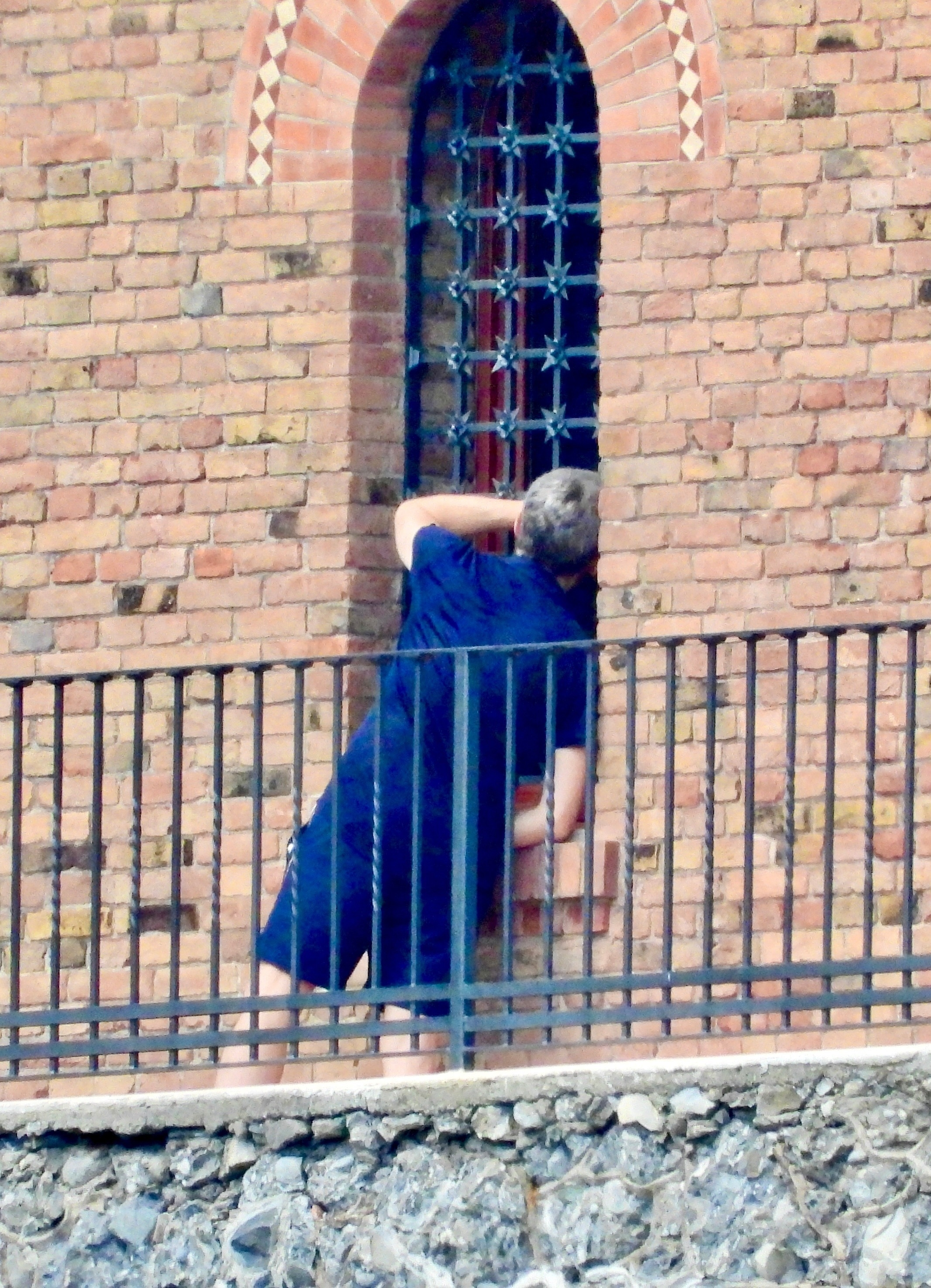 Mystery man leaning into a barred window from a balcony.