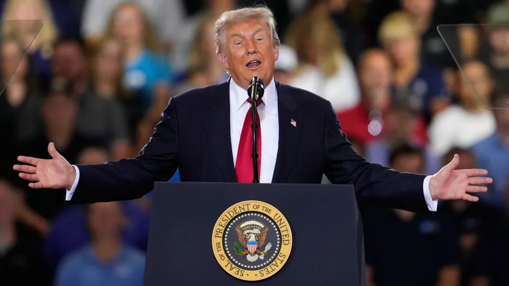 President Donald Trump speaks at a podium with his arms outstretched.