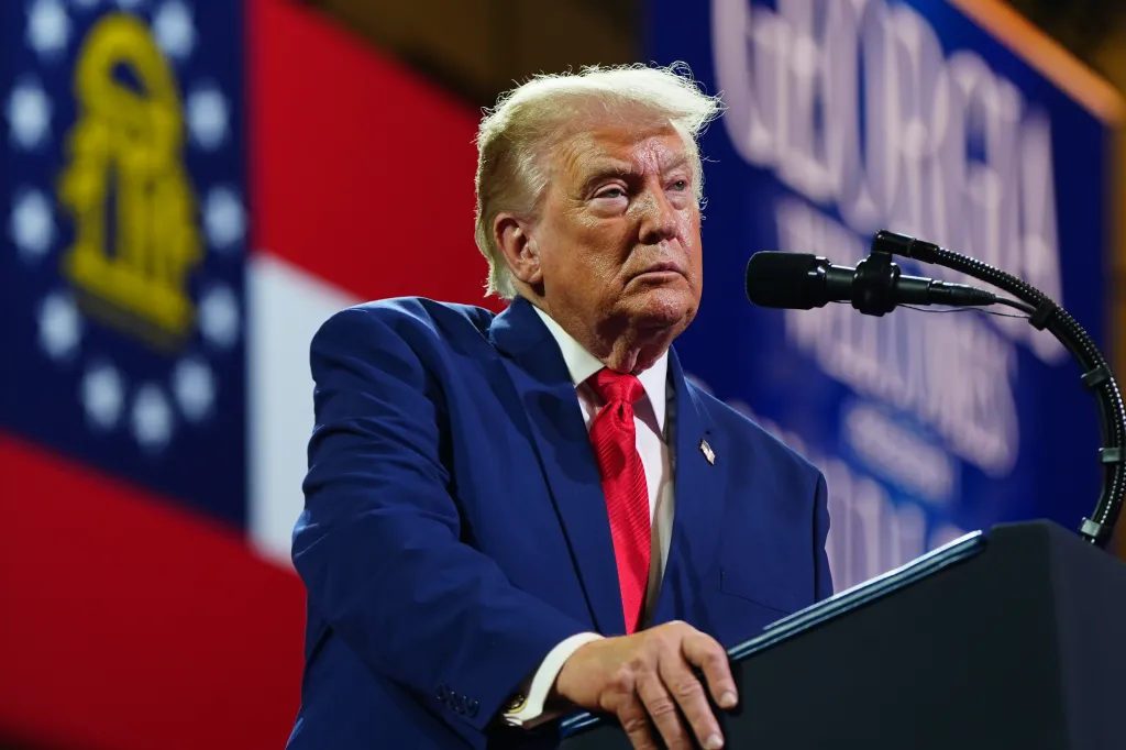 Donald Trump speaking at a podium with a Georgia flag in the background.