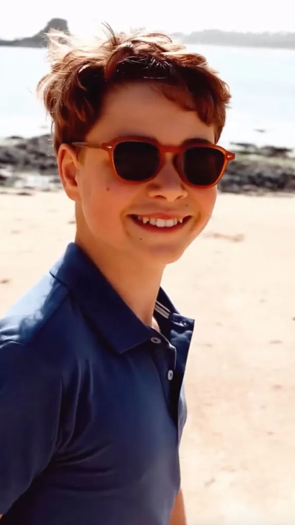 Prince George smiling on a beach while wearing sunglasses and a blue polo shirt.