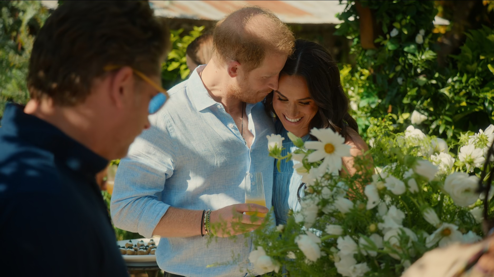 Prince Harry and Meghan Markle embrace at a outdoor gathering.