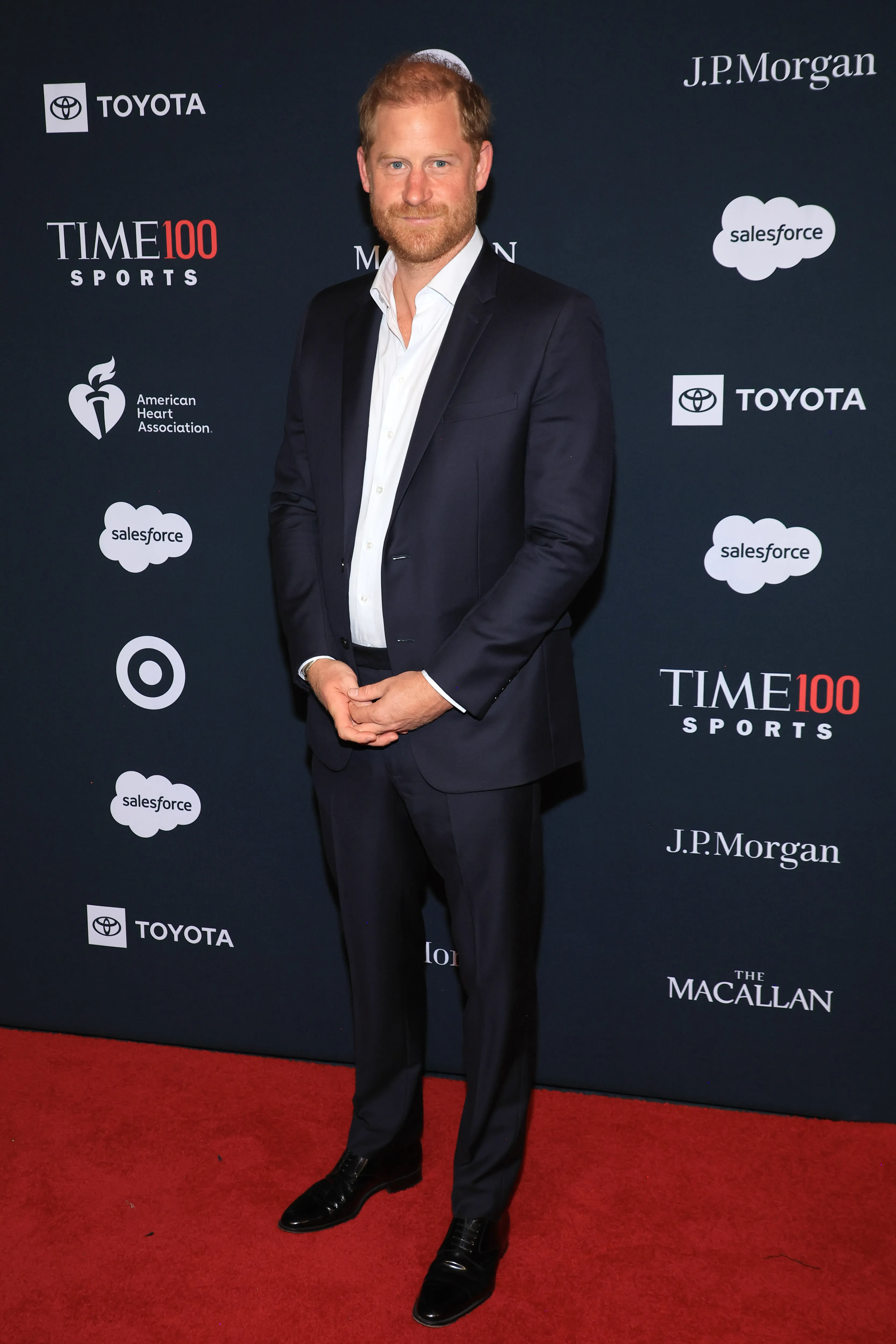 Prince Harry, Duke of Sussex, in a suit, stands on a red carpet at the TIME100 Sports Gala.
