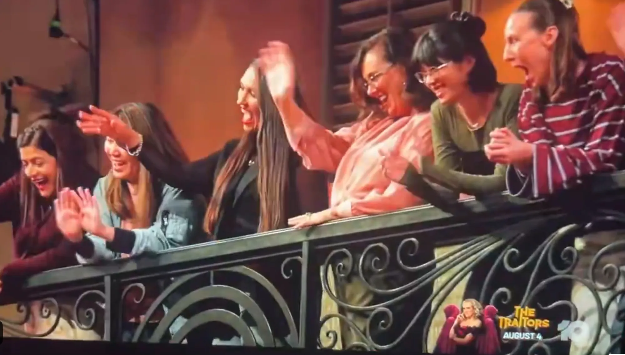 Six women in a balcony cheering and waving.