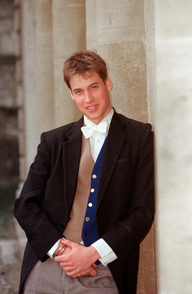 Prince William in a formal school uniform, including a tailcoat, bow tie, and a blue waistcoat, leaning against a stone wall.