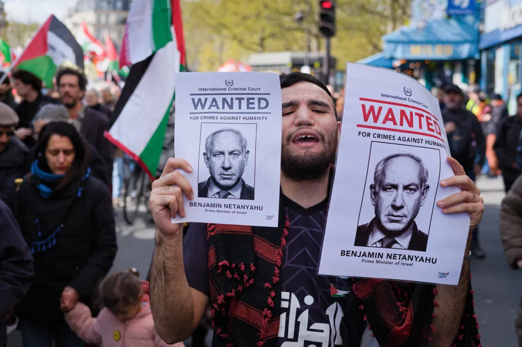 Protester holding "Wanted for crimes against humanity" posters featuring Benjamin Netanyahu at a march.