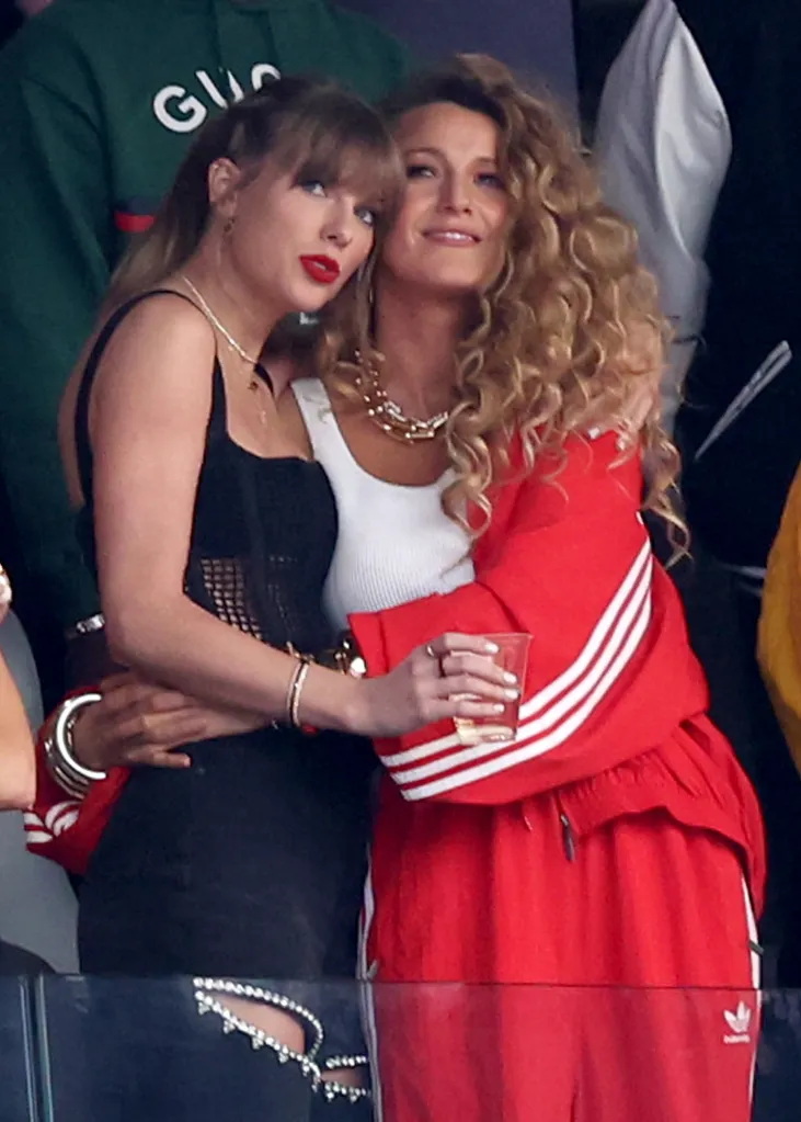 Singer Taylor Swift with red lipstick and actress Blake Lively with curly hair embrace at Super Bowl LVIII.