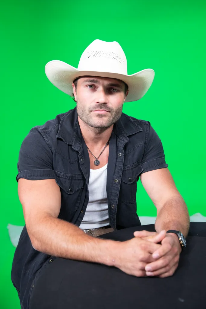 Steven McBee Jr. from McBee Dynasty: Real American Cowboys, wearing a white cowboy hat and black shirt, against a green background.