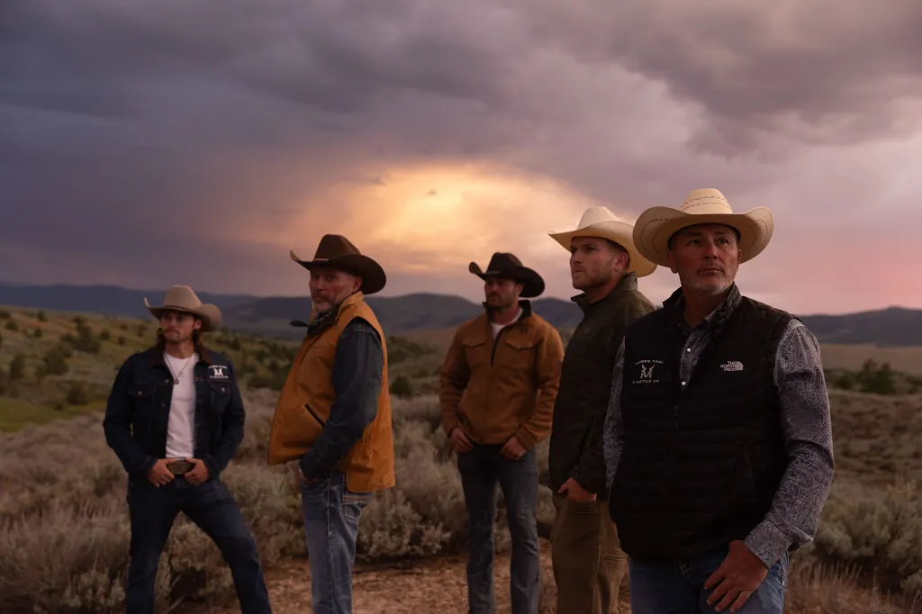 Five cowboys, the McBee family, stand outdoors under a cloudy purple and orange sunset.