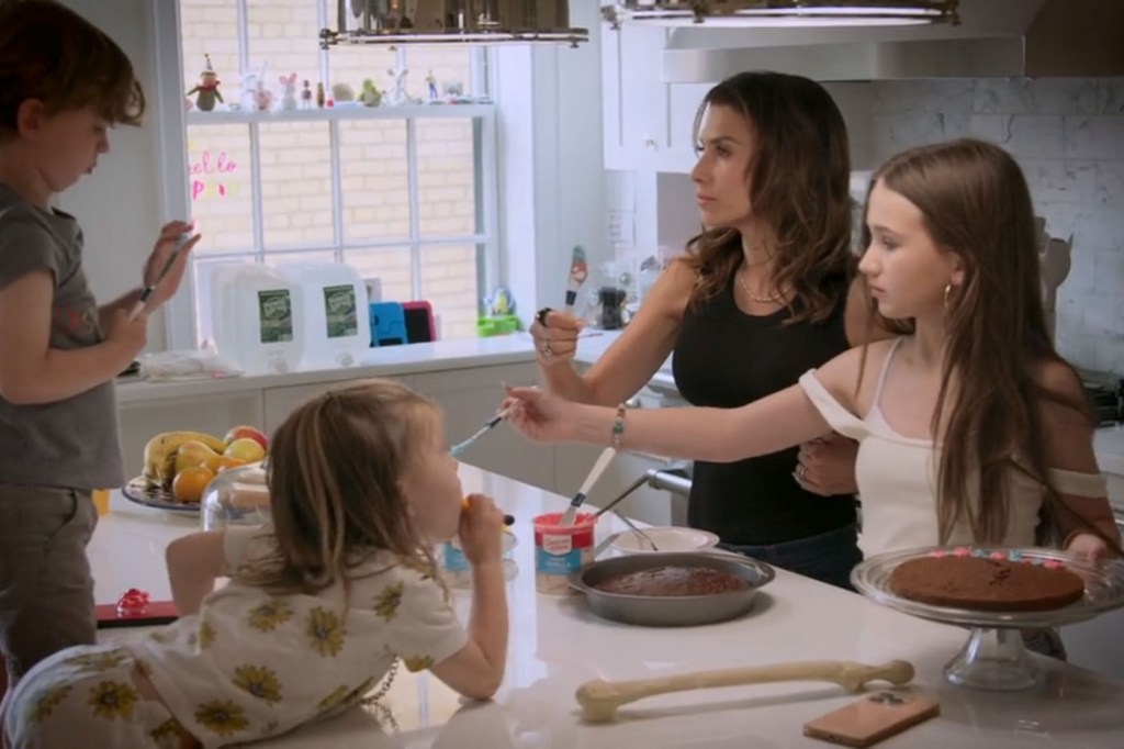 A woman and three children in a kitchen decorating a cake.