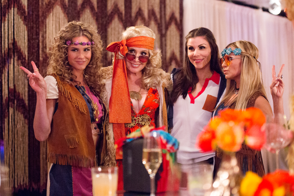 Four women, Meghan King Edmonds, Shannon Beador, Heather Dubrow, and Tamra Barney, in hippie-themed outfits and accessories.