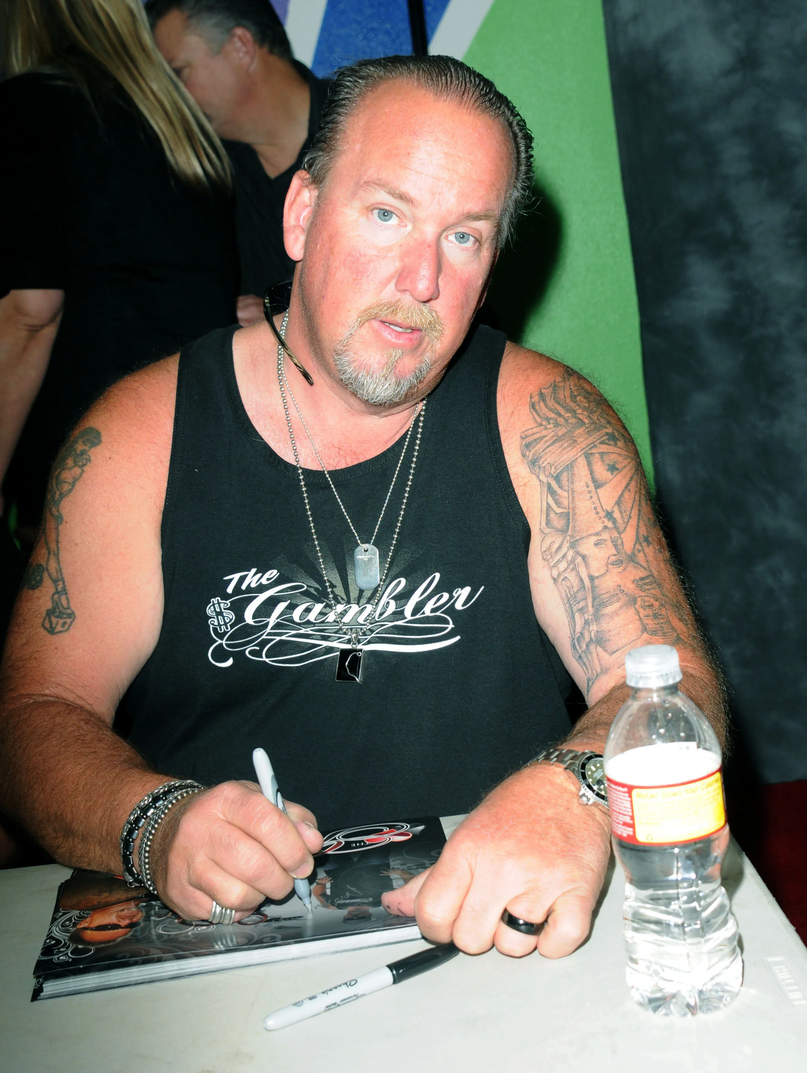 Darrell Sheets in a black tank top and dog tags, signing an autograph.