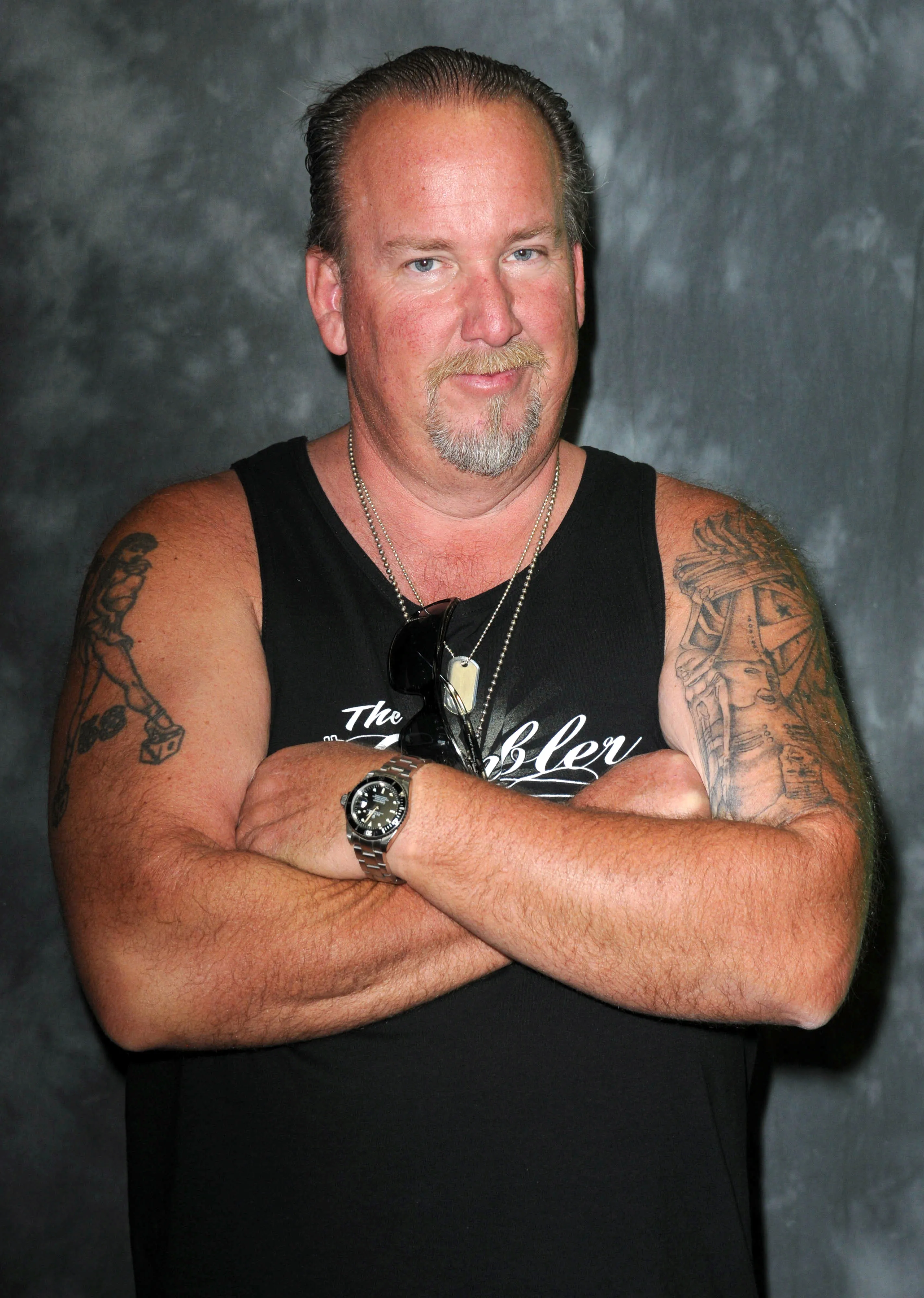 Darrell Sheets in a black tank top, with arms crossed and tattoos on both arms.