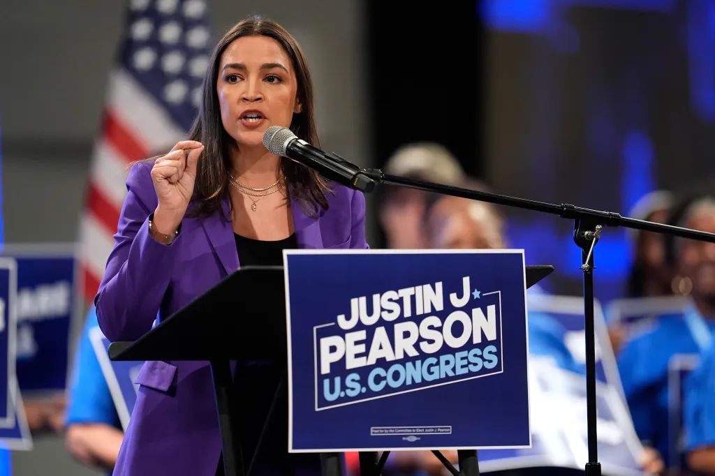 Alexandria Ocasio-Cortez speaking at a rally for Justin J. Pearson, with a "Justin J. Pearson U.S. Congress" sign in the foreground.
