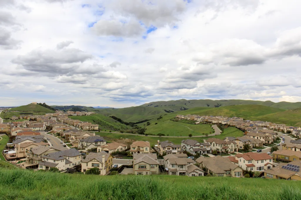 Residential homes in Dublin Hills, California, surrounded by green hills under a cloudy sky.