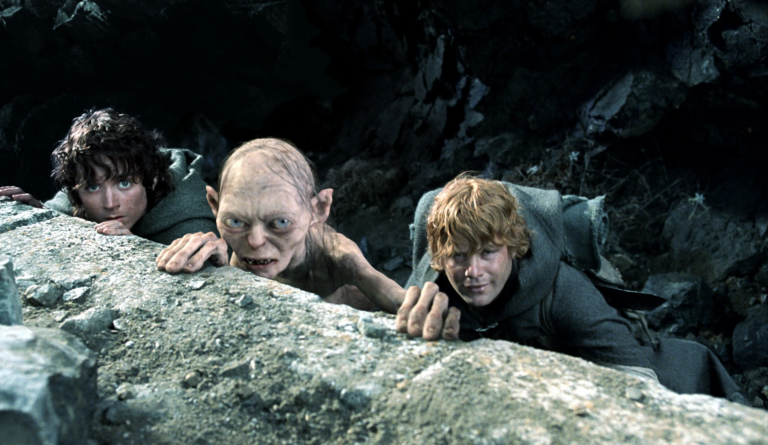 Frodo, Gollum, and Sam peering over a rock.