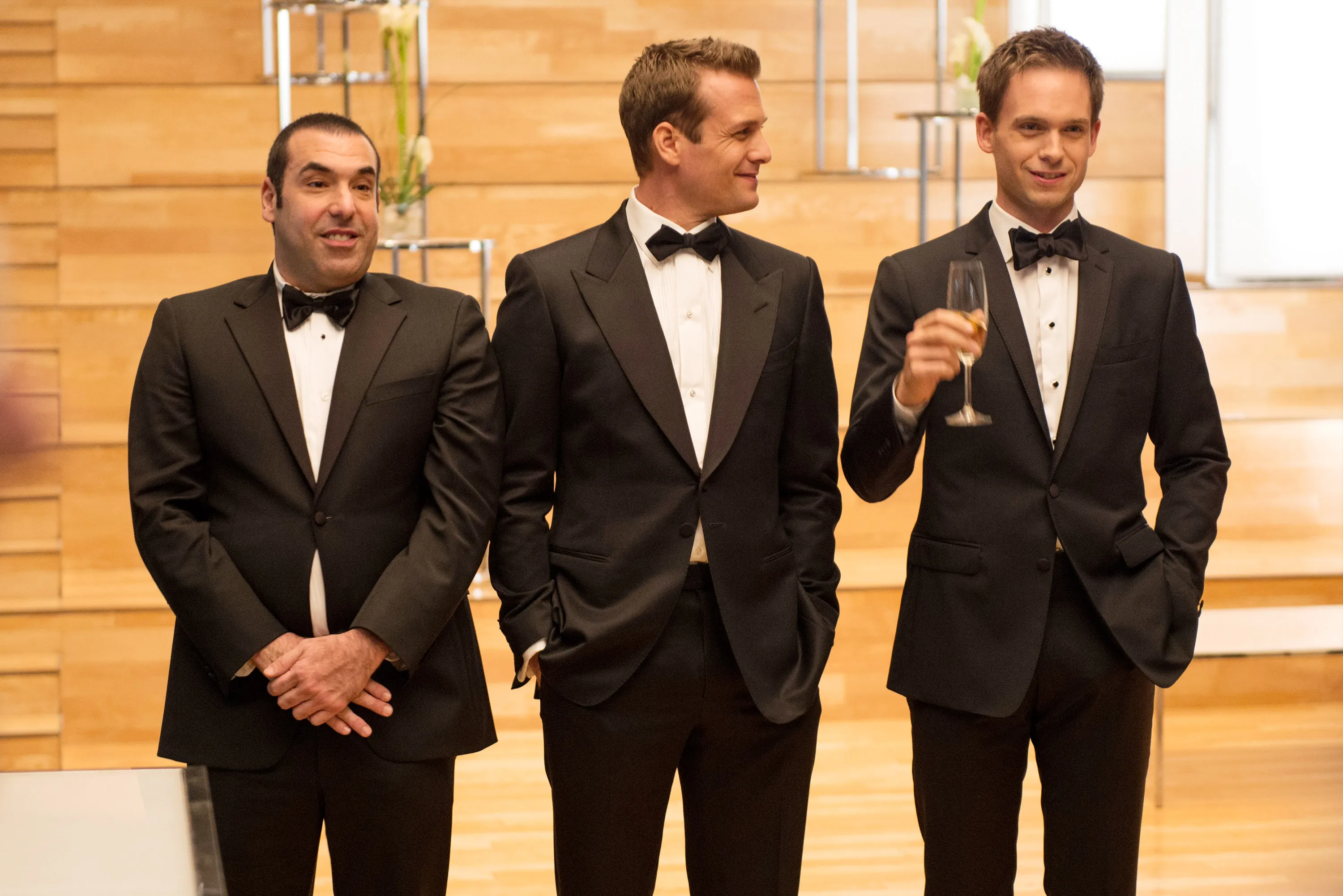 Rick Hoffman, Gabriel Macht, and Patrick J. Adams in tuxedos, with Adams holding a champagne glass.