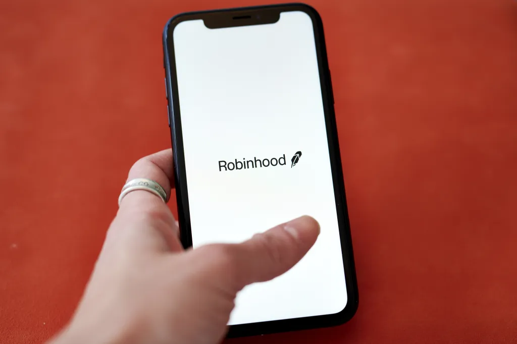A hand holding a smartphone displaying the Robinhood logo.