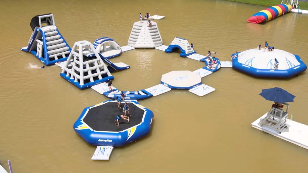 Kids playing on a large inflatable water obstacle course in a lake.