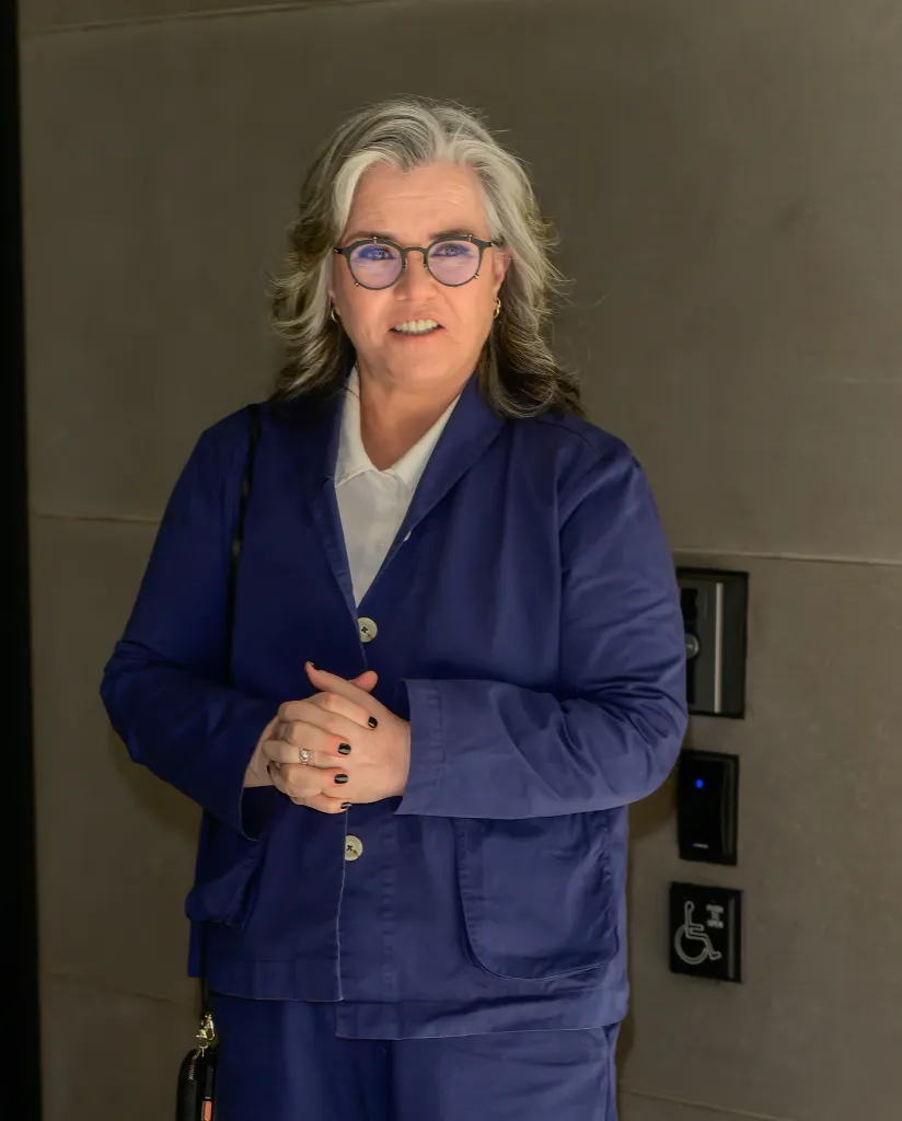 Rosie O'Donnell in a blue suit and glasses.