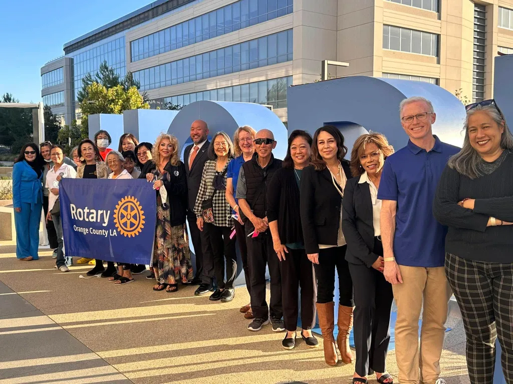 A group of people holding a "Rotary Orange County LA" banner in front of large blue letters.