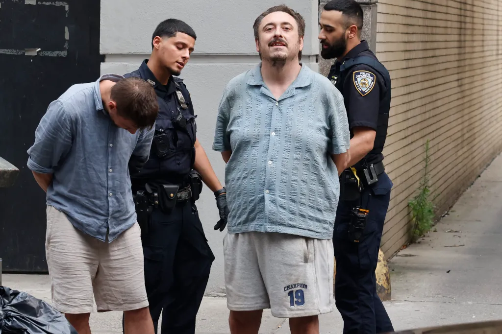 Andrew Truelove, in a blue shirt, is flanked by two NYPD officers after being arrested for allegedly shouting racist slurs during a live broadcast.