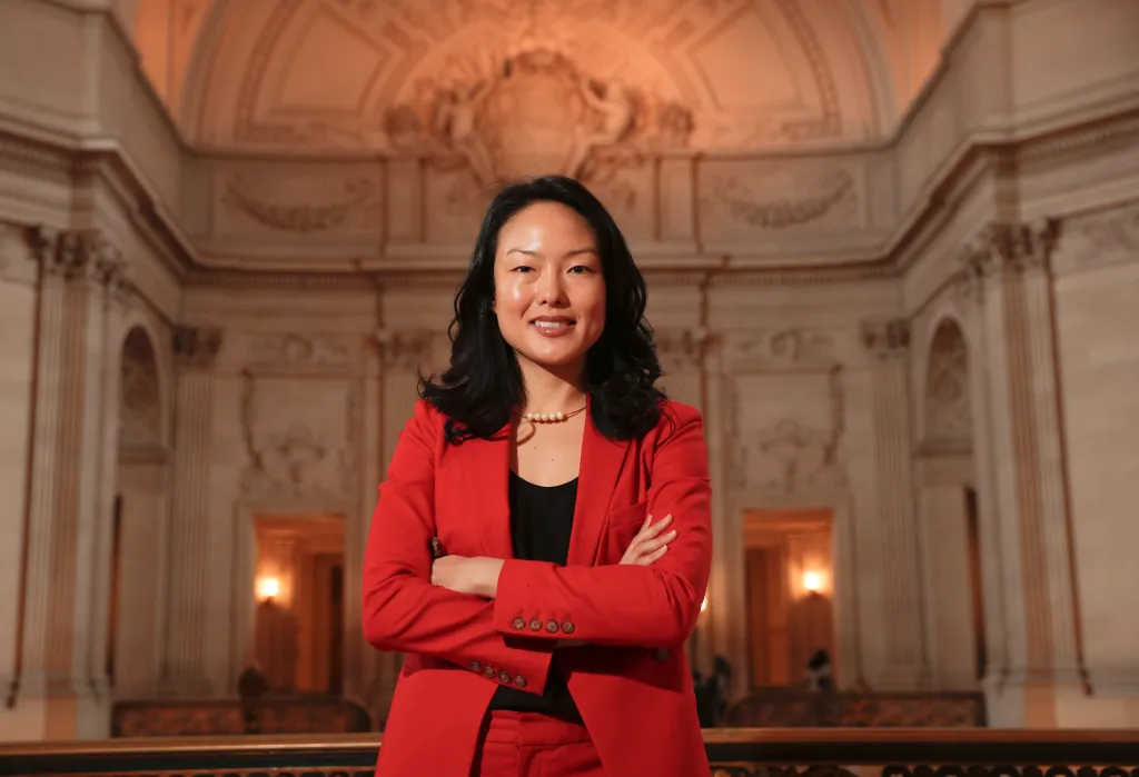San Francisco Supervisor Jane Kim in a red suit jacket posing in City Hall.