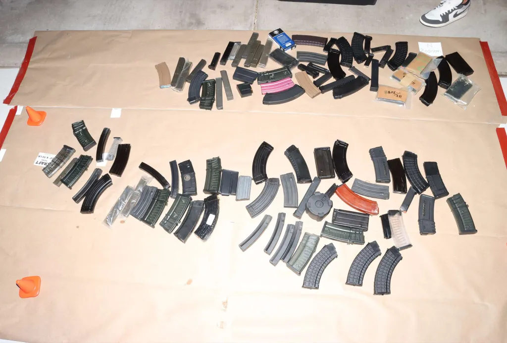 A collection of various firearm magazines laid out on brown paper, including curved and straight designs, with some items individually packaged in clear plastic.
