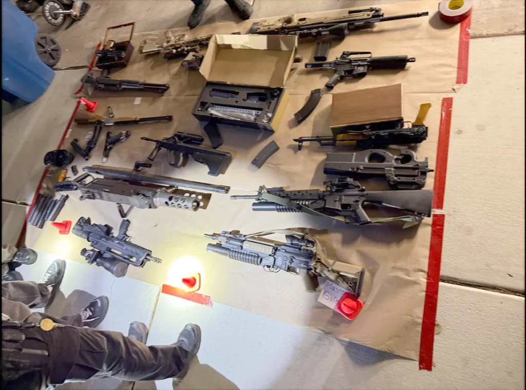A large collection of firearms and ammunition confiscated and laid out on a tarp, including rifles, submachine guns, and handguns.