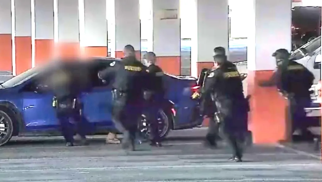 Police officers apprehending suspects around a blue car.