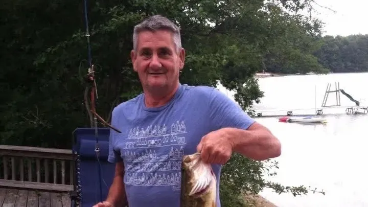 Scott "Scooter" Winslow holding a large bass fish with a lake in the background.