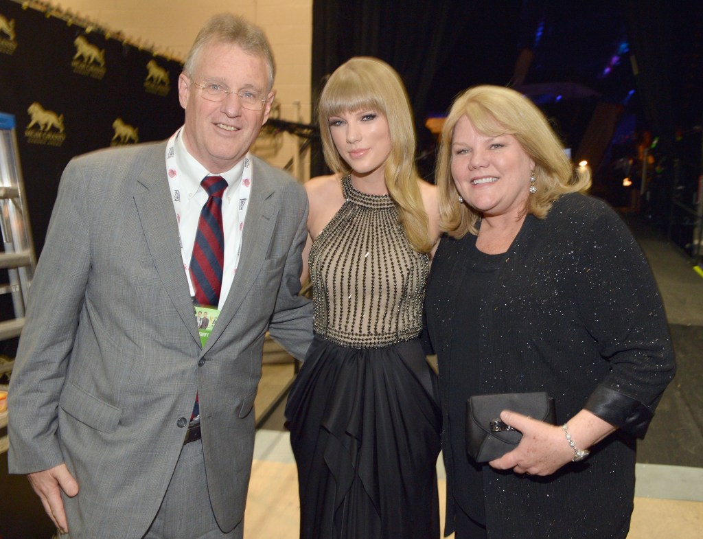 Taylor Swift, in a black dress with sequins, with her parents Scott Swift, in a grey suit and red and blue striped tie, and Andrea Swift, in a black cardigan and black dress, at the 48th Annual Academy of Country Music Awards.