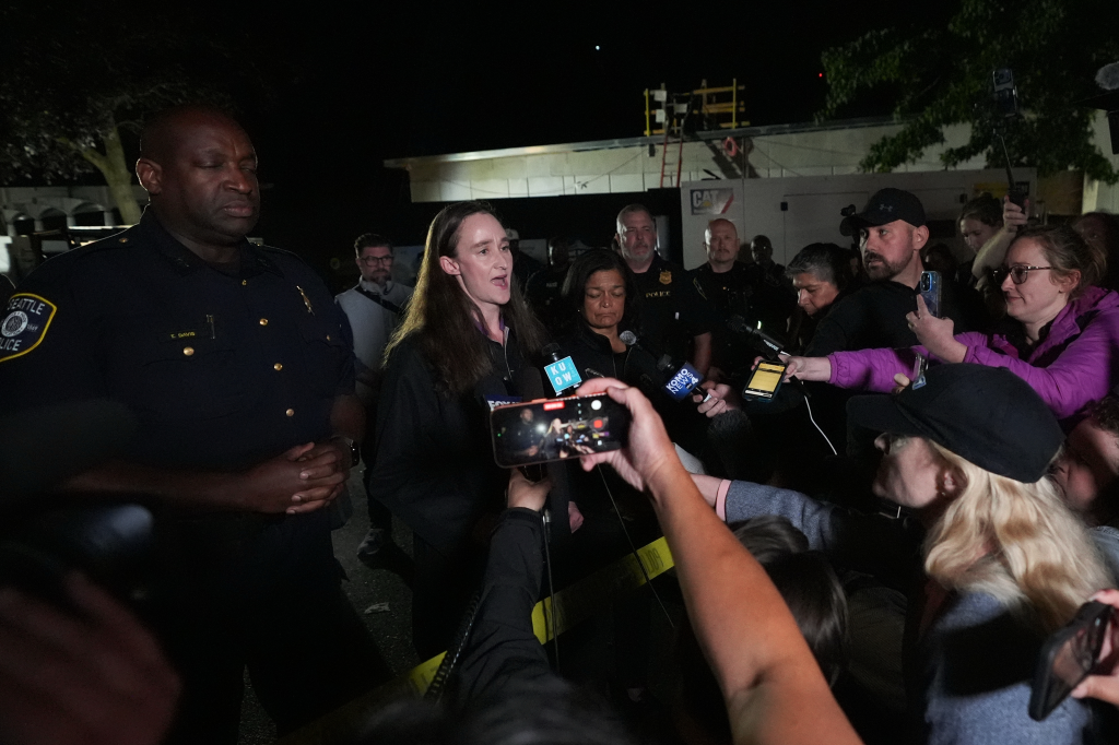 Seattle Mayor Katie Wilson speaks at a news conference surrounded by reporters and police officers.