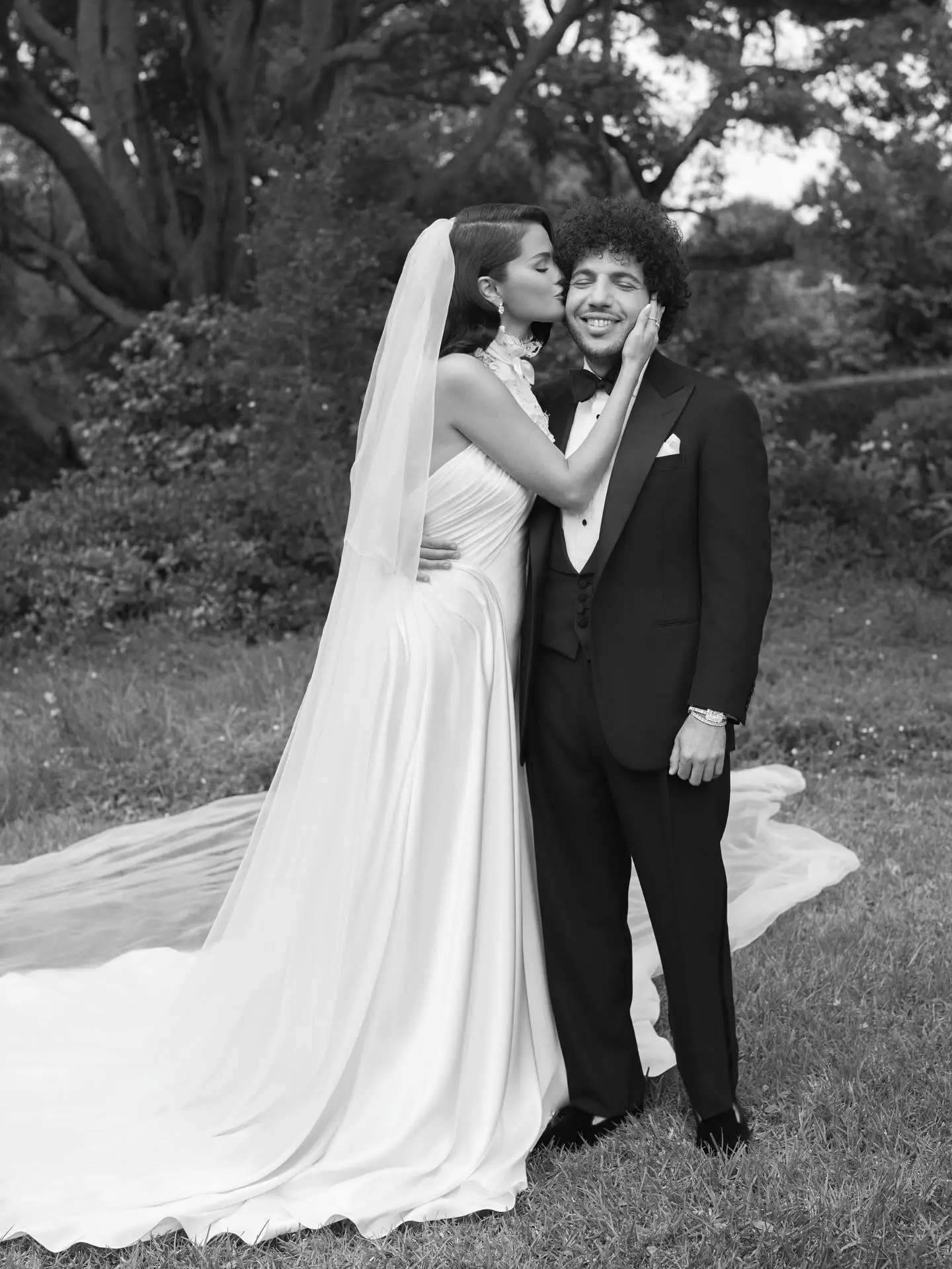 Selena Gomez kissing Benny Blanco on the cheek while wearing a wedding gown and veil.