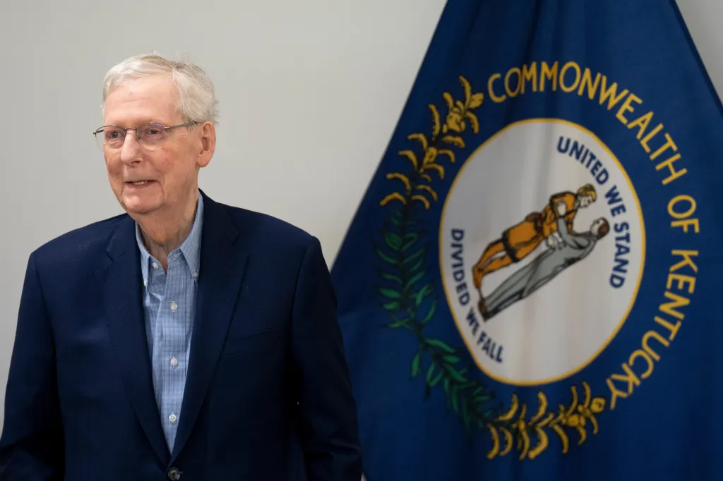 Senator Mitch McConnell speaking at a press conference in front of the Kentucky state flag.