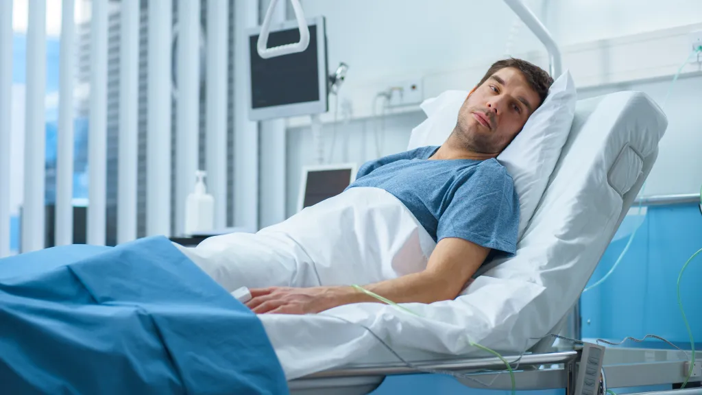 Man lying in a hospital bed with medical monitors and equipment visible.